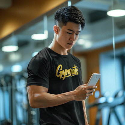 Man wearing a black 'Gymrats' t-shirt using a phone in a gym setting